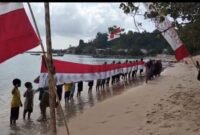 Masyarakat bersama generasi muda Desa Gemia membentangkan bendera Merah Putih raksasa sepanjang 45 meter di pesisir pantai. || dok : Kasedata